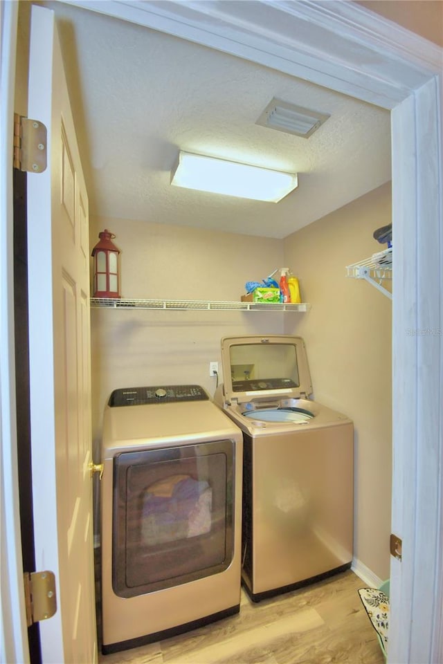 laundry area with laundry area, washing machine and clothes dryer, and light wood-style flooring