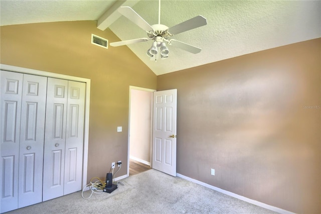 unfurnished bedroom with vaulted ceiling with beams, a textured ceiling, light colored carpet, visible vents, and a closet