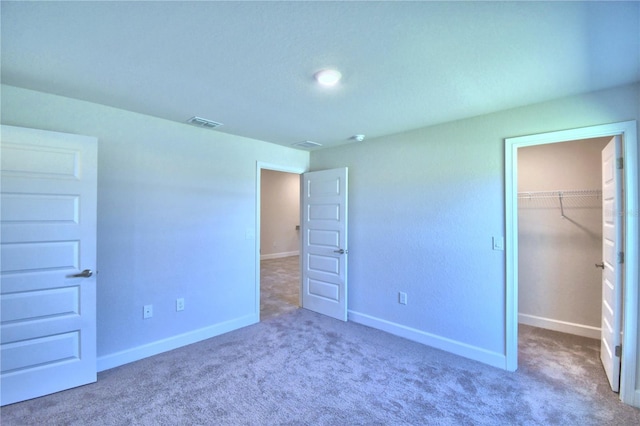 unfurnished bedroom featuring a walk in closet, a closet, and carpet floors