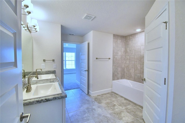 bathroom with vanity, a textured ceiling, and tiled shower / bath