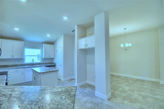 kitchen featuring light stone countertops, a kitchen island, pendant lighting, a chandelier, and white cabinetry