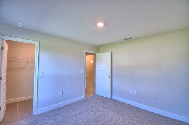 unfurnished bedroom with carpet, a walk in closet, and a closet