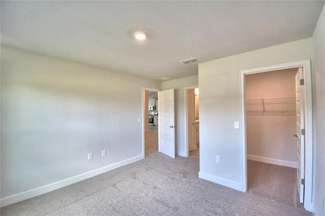 unfurnished bedroom featuring a walk in closet, light colored carpet, and a closet