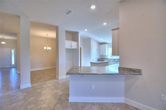 kitchen featuring dark stone counters, kitchen peninsula, hanging light fixtures, a notable chandelier, and white cabinetry