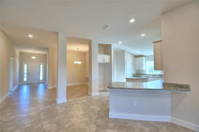 kitchen with an inviting chandelier, light stone counters, kitchen peninsula, decorative light fixtures, and white cabinets