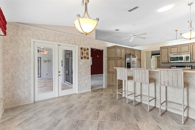 kitchen with lofted ceiling, french doors, ceiling fan, a kitchen bar, and stainless steel appliances