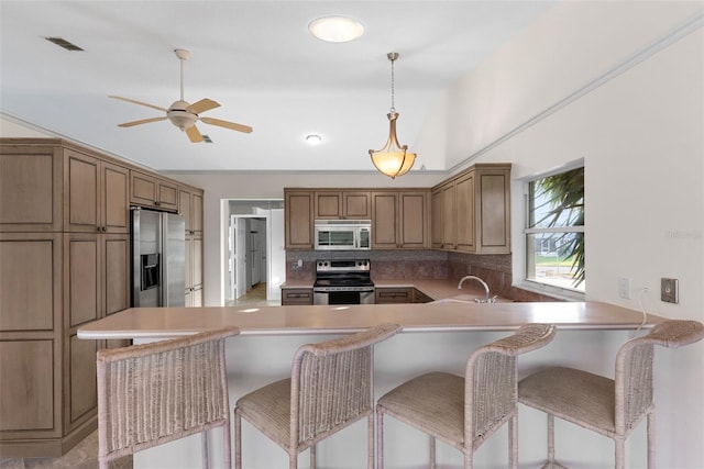 kitchen with sink, a breakfast bar, appliances with stainless steel finishes, backsplash, and kitchen peninsula