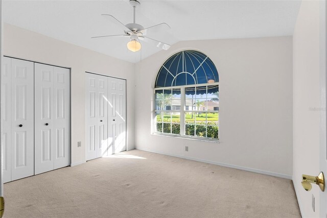 unfurnished bedroom featuring light carpet, ceiling fan, lofted ceiling, and multiple closets