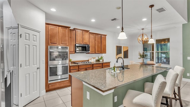 kitchen featuring light stone countertops, appliances with stainless steel finishes, a center island with sink, and sink