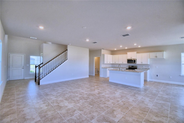 kitchen with appliances with stainless steel finishes, a kitchen island with sink, sink, light tile patterned floors, and white cabinets