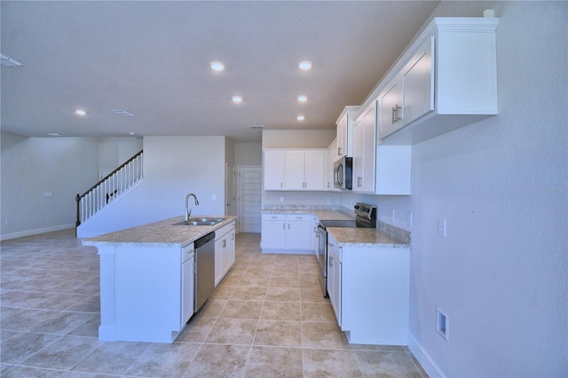 kitchen with light stone counters, stainless steel appliances, a kitchen island with sink, sink, and white cabinets