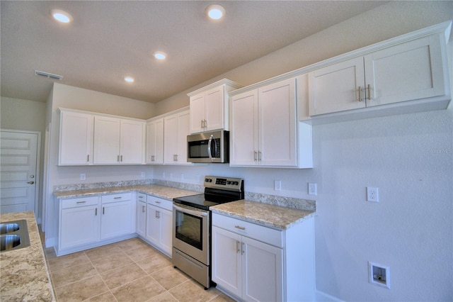 kitchen with appliances with stainless steel finishes, light stone counters, sink, light tile patterned floors, and white cabinetry