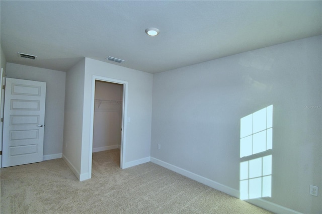 unfurnished bedroom with a spacious closet, light carpet, and a closet