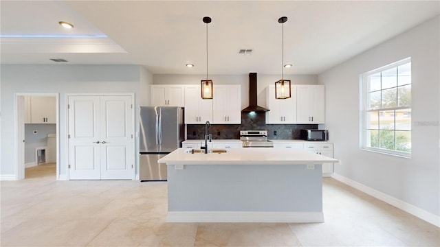 kitchen with stainless steel appliances, wall chimney range hood, decorative light fixtures, a kitchen island with sink, and white cabinets