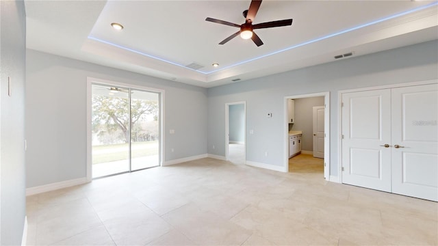 unfurnished bedroom featuring a raised ceiling, ensuite bathroom, ceiling fan, and access to outside