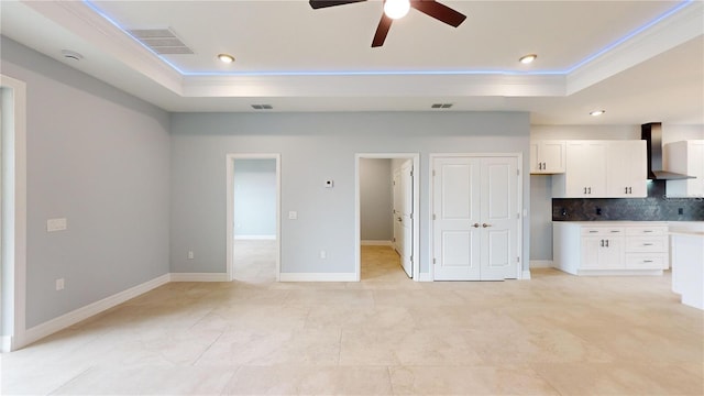 unfurnished living room featuring a raised ceiling, ceiling fan, light tile patterned floors, and ornamental molding