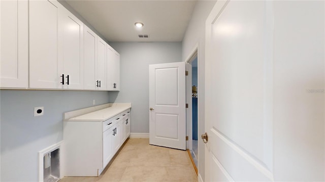 laundry room featuring electric dryer hookup, cabinets, and light tile patterned floors