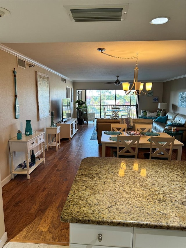 kitchen featuring light stone countertops, dark wood-type flooring, decorative light fixtures, white cabinets, and ornamental molding