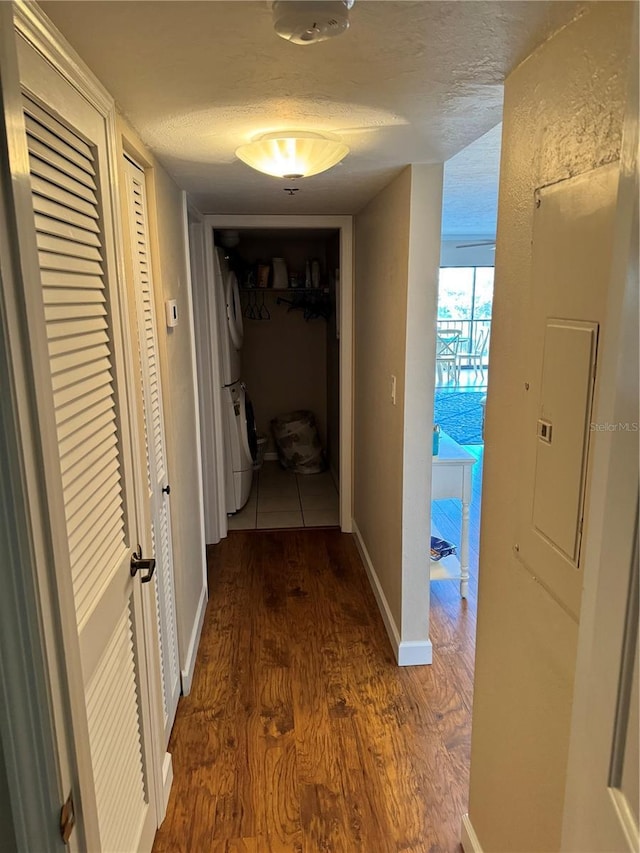 corridor featuring stacked washer / dryer, dark hardwood / wood-style flooring, a textured ceiling, and electric panel