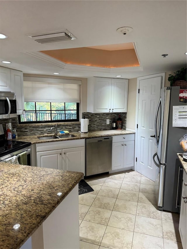 kitchen featuring appliances with stainless steel finishes, a raised ceiling, sink, dark stone countertops, and white cabinetry