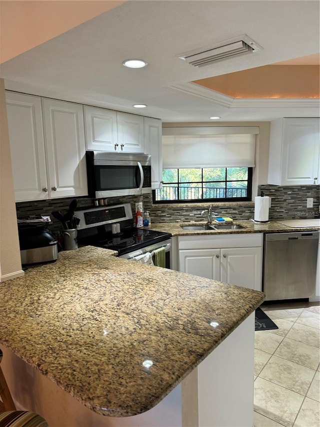 kitchen with kitchen peninsula, appliances with stainless steel finishes, decorative backsplash, sink, and white cabinetry