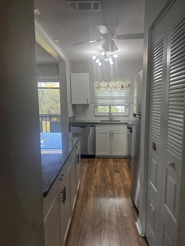 kitchen with visible vents, dark wood-type flooring, a sink, dark stone counters, and dishwasher