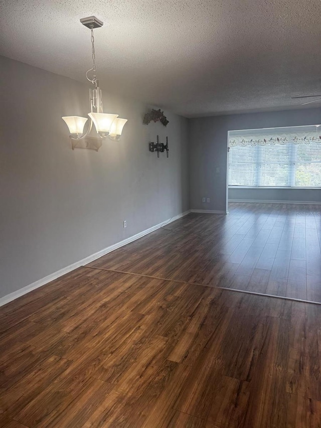 empty room featuring a textured ceiling, baseboards, and dark wood-type flooring