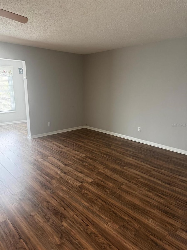 spare room featuring dark wood-type flooring, a textured ceiling, baseboards, and a ceiling fan