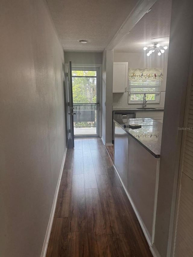 hall with dark wood-type flooring, a sink, a textured ceiling, and baseboards