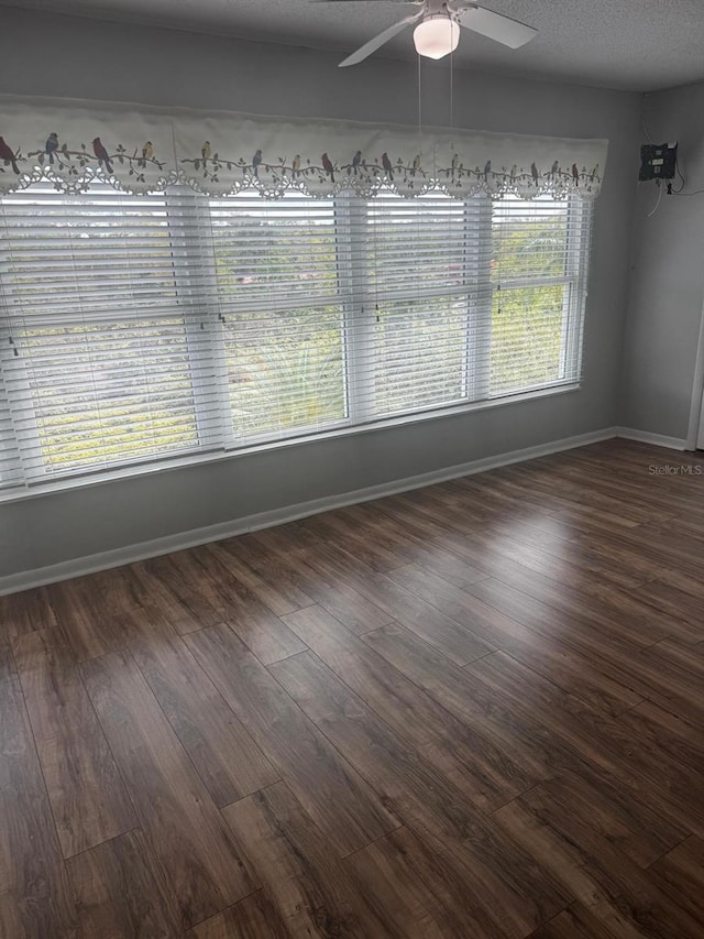 empty room with a textured ceiling, wood finished floors, a ceiling fan, and baseboards