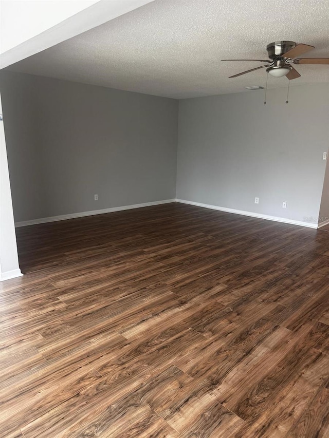 empty room with ceiling fan, baseboards, dark wood finished floors, and a textured ceiling