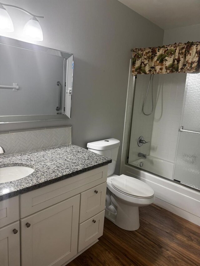 full bathroom featuring toilet, bath / shower combo with glass door, wood finished floors, and vanity