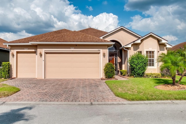 ranch-style house with a garage, roof with shingles, decorative driveway, a front yard, and stucco siding