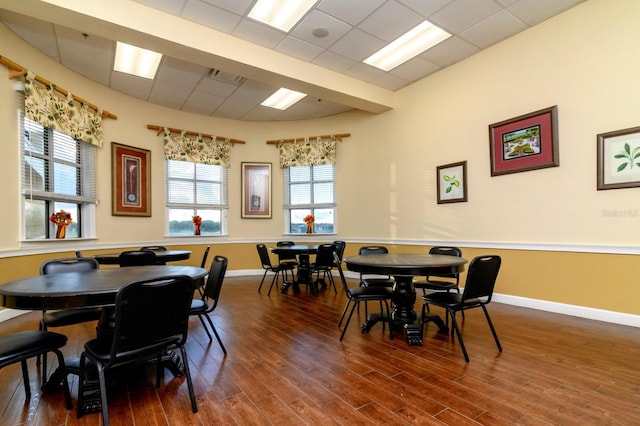 dining space with a drop ceiling, visible vents, baseboards, and wood finished floors