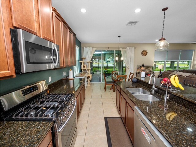 kitchen with light tile patterned floors, stainless steel appliances, a sink, brown cabinets, and decorative light fixtures