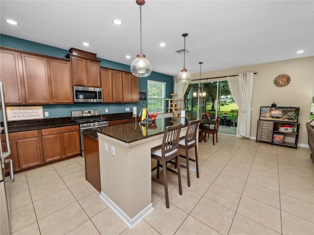 kitchen featuring light tile patterned flooring, stainless steel appliances, hanging light fixtures, brown cabinets, and dark stone countertops