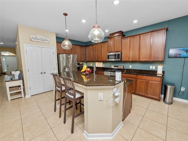 kitchen with light tile patterned floors, recessed lighting, appliances with stainless steel finishes, brown cabinetry, and dark stone countertops