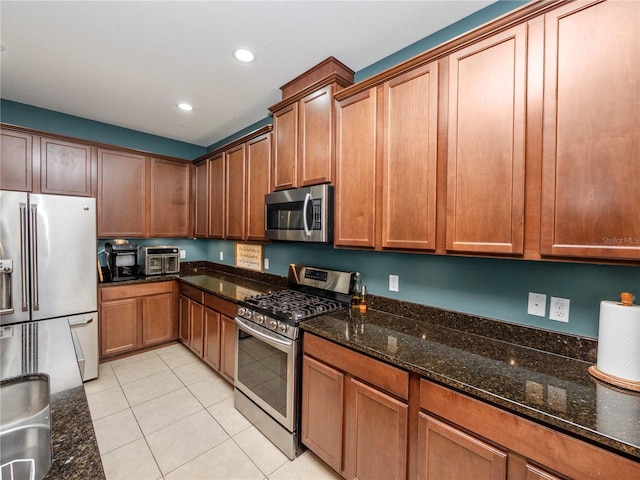 kitchen featuring light tile patterned floors, recessed lighting, appliances with stainless steel finishes, brown cabinets, and dark stone counters