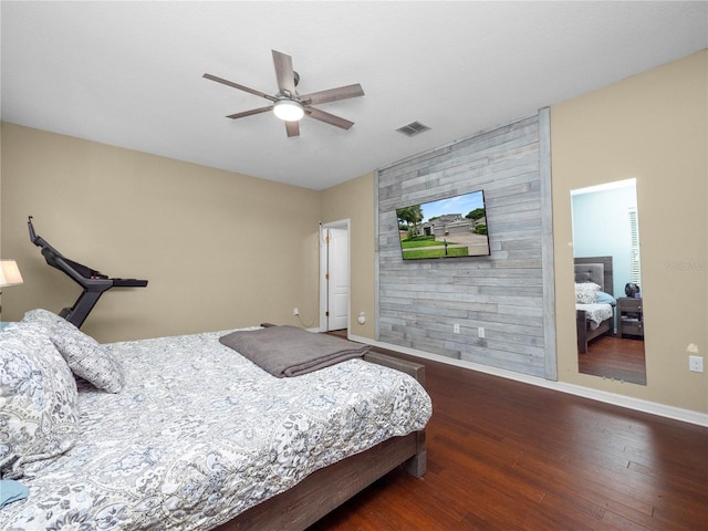 bedroom with ceiling fan, an accent wall, wood finished floors, visible vents, and baseboards