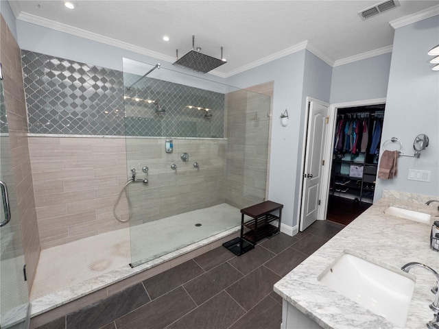 bathroom with crown molding, visible vents, a tile shower, and a sink