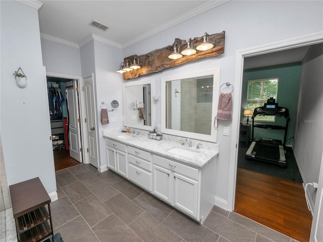 bathroom with double vanity, visible vents, a walk in closet, crown molding, and a sink