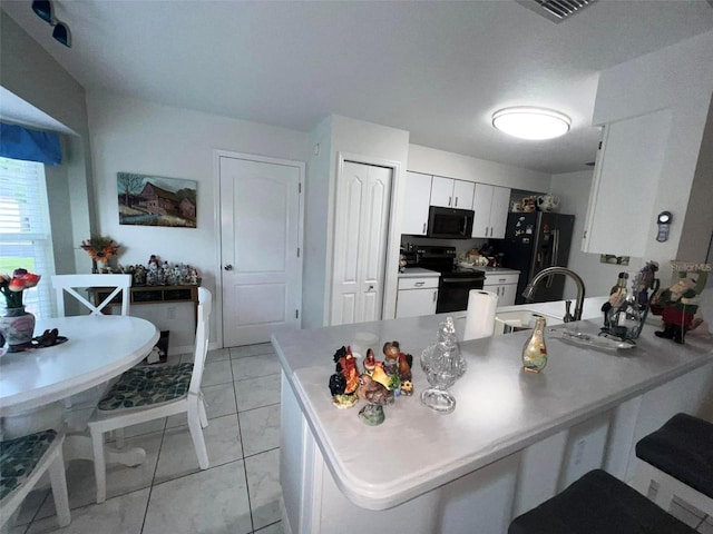 kitchen with black appliances, sink, kitchen peninsula, light tile patterned floors, and white cabinetry