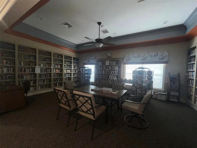 carpeted dining space featuring a tray ceiling, ceiling fan, built in features, and ornamental molding