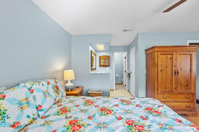 tiled bedroom featuring ensuite bathroom, ceiling fan, and a textured ceiling