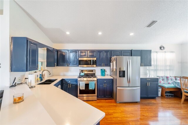 kitchen featuring sink, stainless steel appliances, a textured ceiling, blue cabinets, and light wood-type flooring