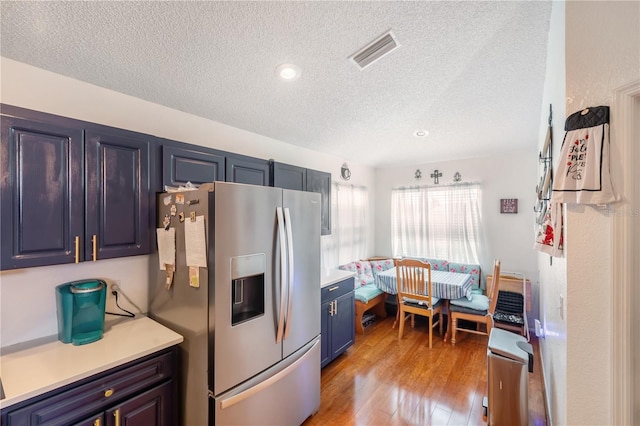 kitchen with stainless steel fridge, light hardwood / wood-style floors, breakfast area, blue cabinetry, and a textured ceiling