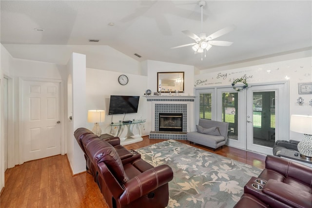 living room featuring a tiled fireplace, wood-type flooring, vaulted ceiling, and french doors