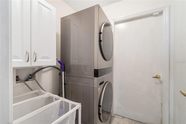 clothes washing area featuring cabinets, stacked washer and clothes dryer, and light tile patterned floors