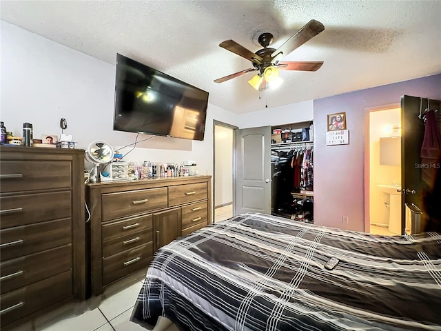 bedroom featuring ensuite bathroom, a closet, light tile patterned floors, a textured ceiling, and ceiling fan