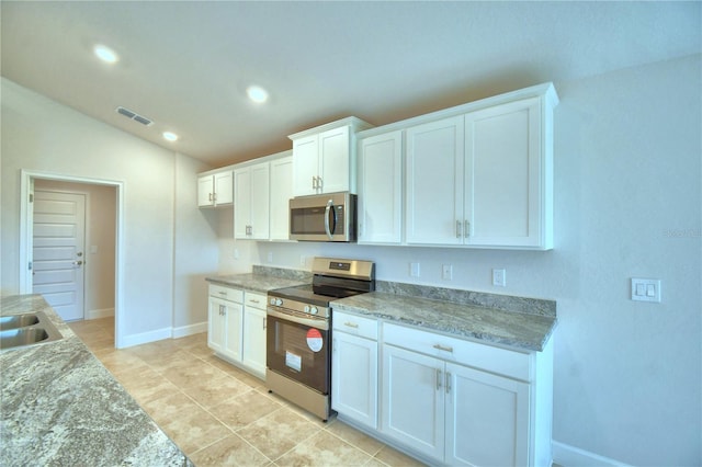 kitchen featuring vaulted ceiling, light tile patterned floors, appliances with stainless steel finishes, light stone counters, and white cabinetry